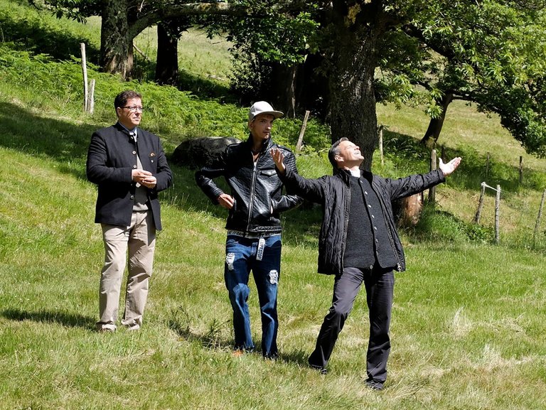 Drei Männer stehen auf einer Wiese - einer genießt die Sonne mit ausgestreckten Armen