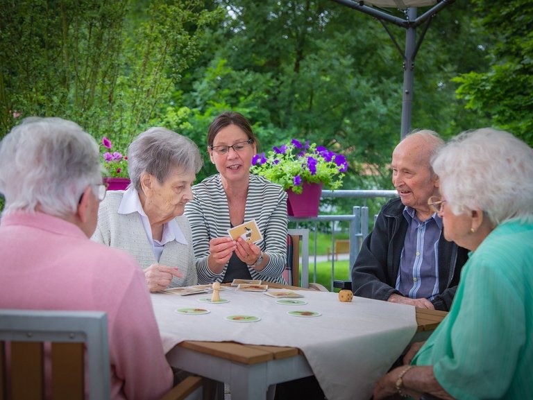 Eine Pflegerin unterstützt Bewohner/innen beim Kartenspiel auf der Terasse