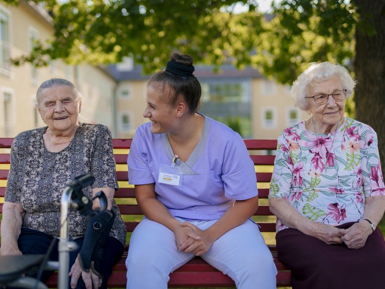 Eine Pflegerin unterstützt Bewohner/innen beim Kartenspiel auf der Terasse