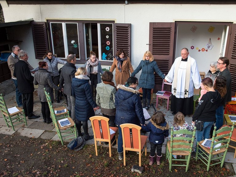 Stuhlkreis auf der Terasse: ein Pater spricht scheinbar ein Gebet - alle stehen und halten sich an den Händen